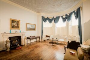 Classic English drawing room with vintage decor, ornate ceiling, and antique furnishings.